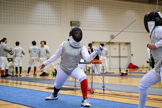 Two fencers are in a midst of a match, the image is primarily focused on the Brock fencer who is in an on-guard position.