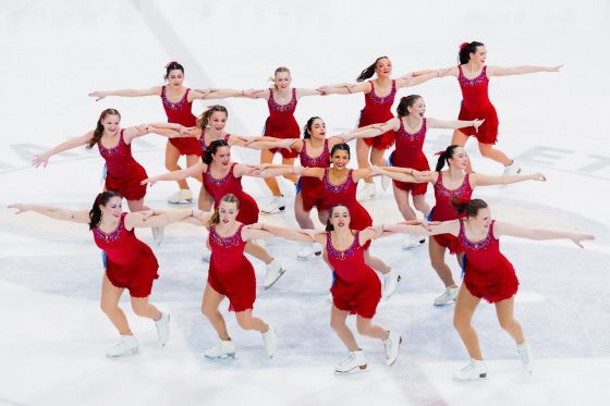 Brock's figure skating team on the ice mid performance - four lines with four skaters linking arms across.