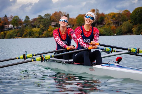 Rowers smiling on a rowboat in water.