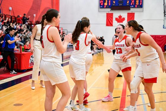 Women's basketball team gathering on the court celebrating with clapping and big smiles.
