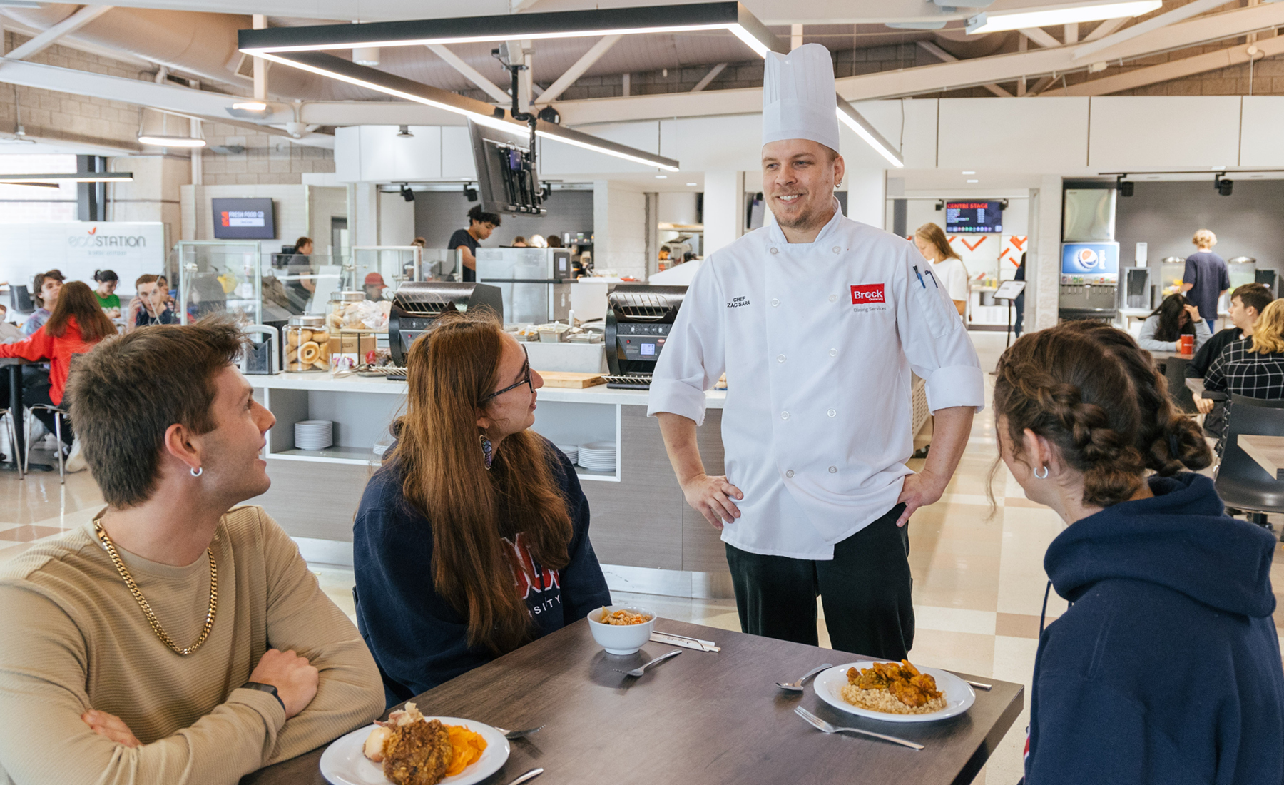 Brock Dining Services Chef Zak Sara talks to students at a table in Decew Dining Hall 