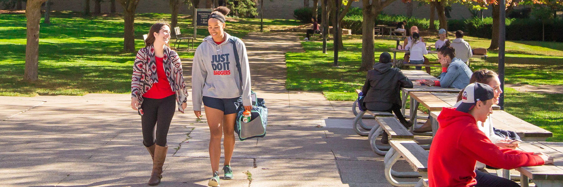 Students walking on campus and some sitting at picnic tables.
