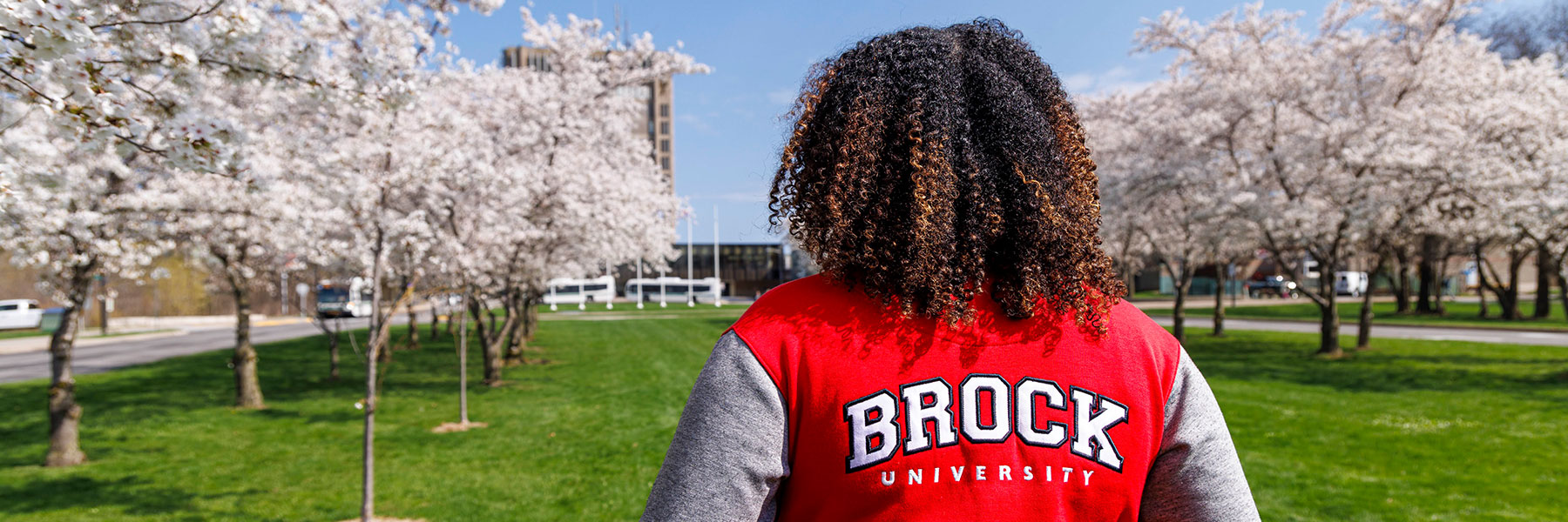 Student with a Brock University jacket on with cherry blossom trees in the background.