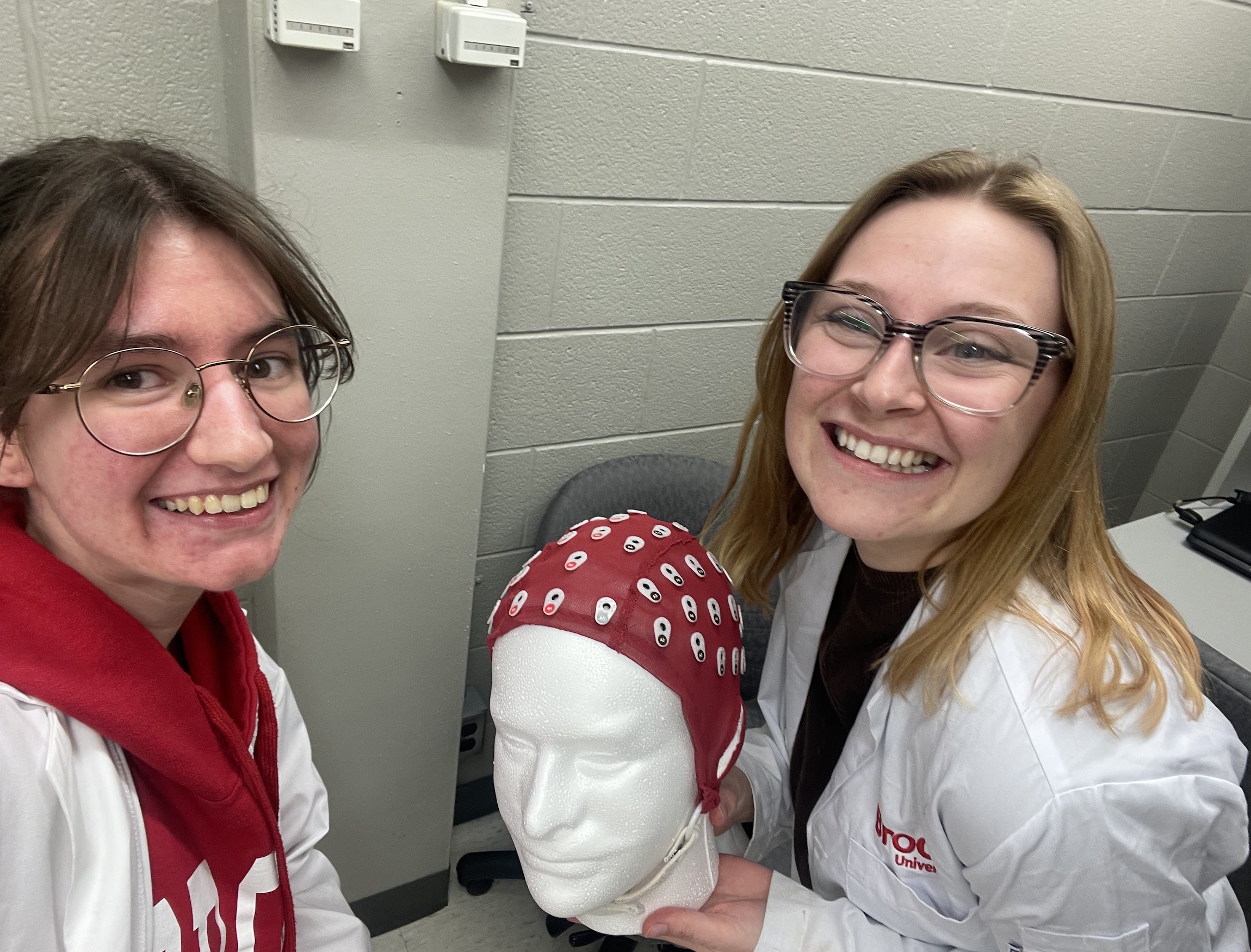 Two students in Brock University white lab coats holding a mannequin head with a device.