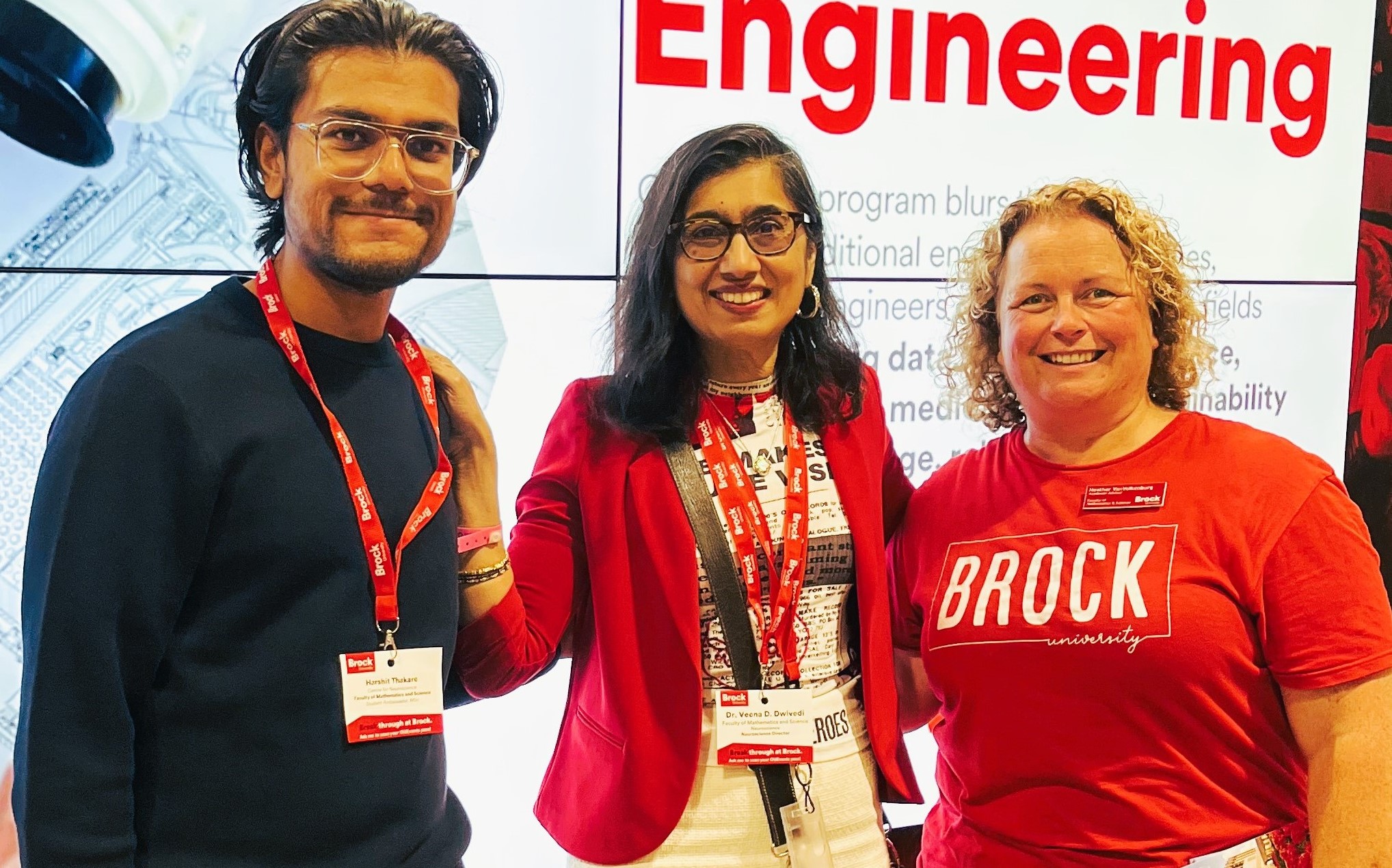 Harshit Thakare, Veena Dwivedi and Heather Van Volkenburg standing together in front of an Engineering digital sign.