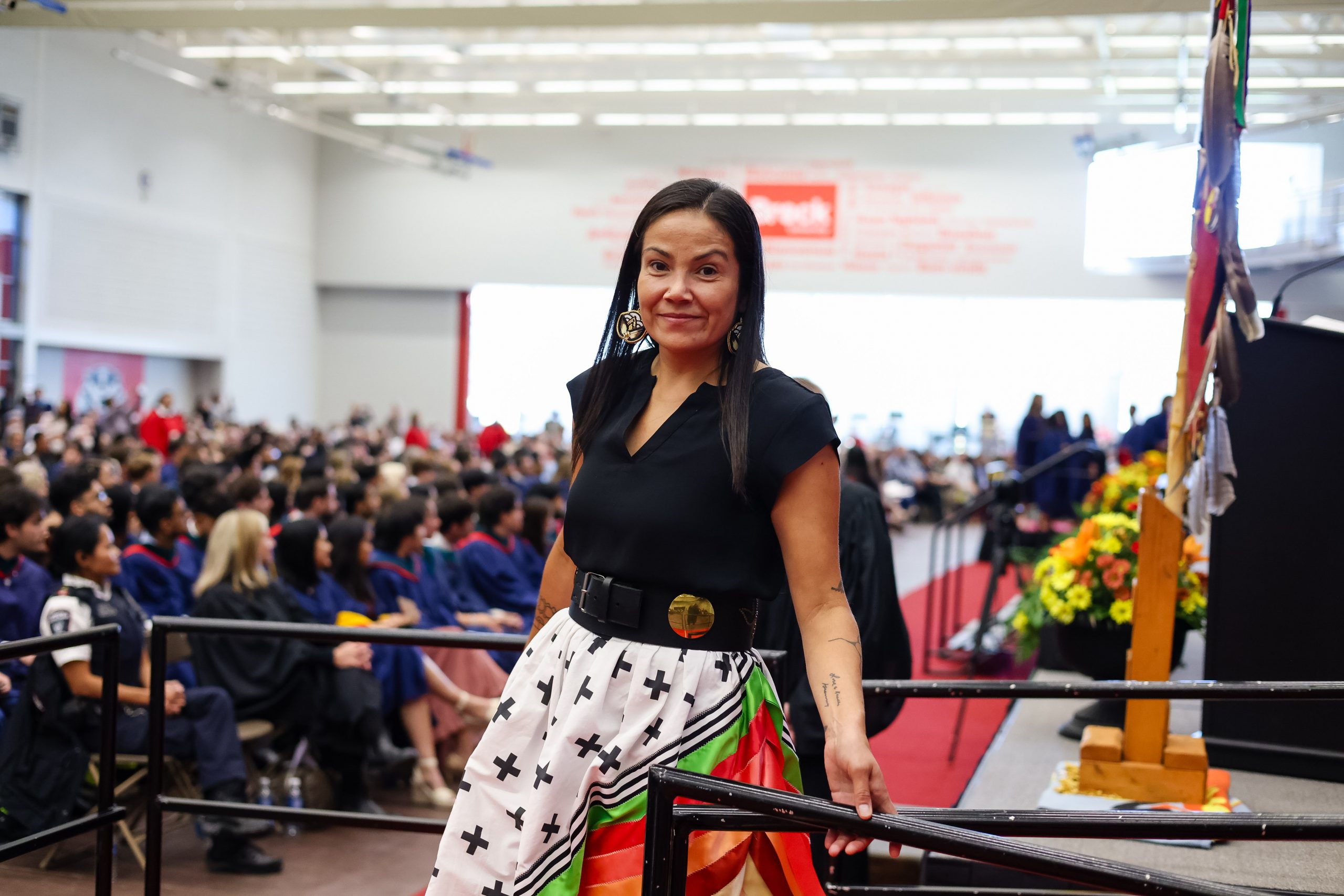 A woman crosses the Convocation stage wearing Indigenous regalia.