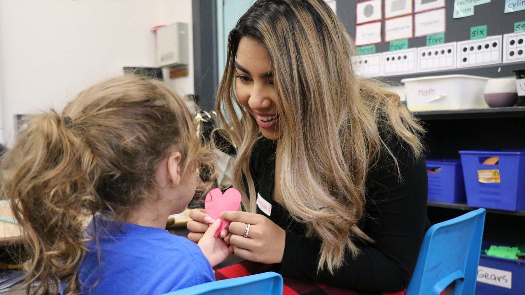 An elementary school student makes a Christmas ornament with a Brock volunteer