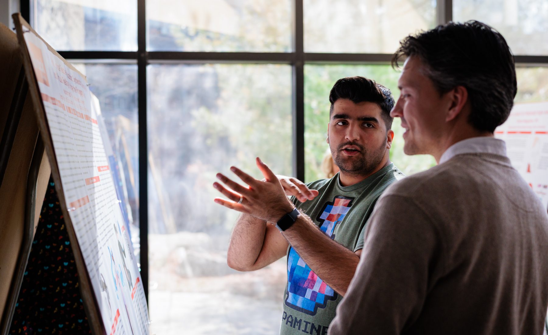 Two men stand in front of a poster talking. 