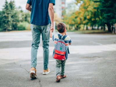 A father holds a child's hand while crossing the street.