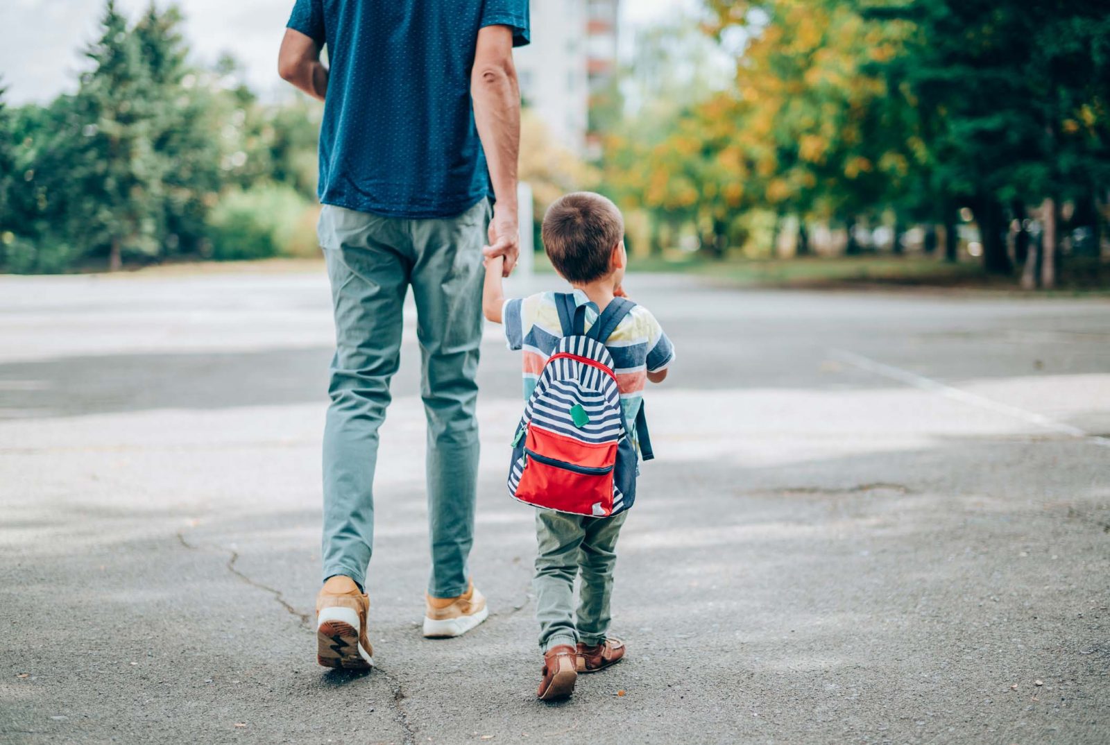 A father holds a child's hand while crossing the street.