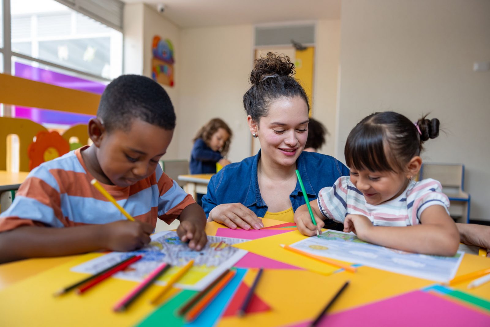 A teacher sits in a classroom with two small children.