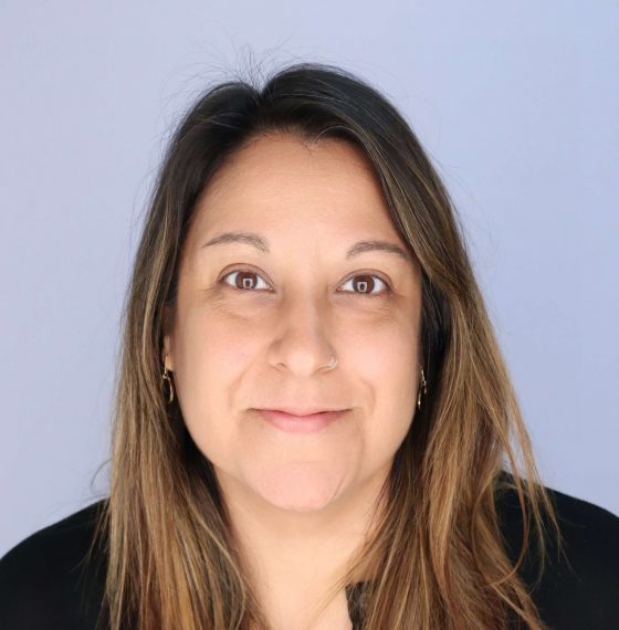 A woman smiles at the camera against a light purple background.