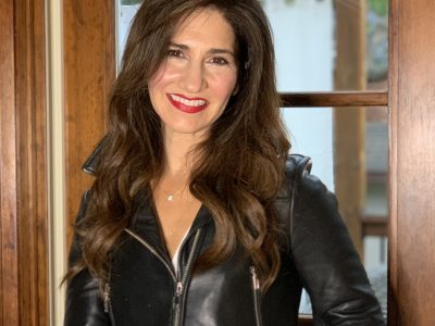 Darlene Ciuffetelli Parker standing in front of a window. She is wearing a white blouse and a cropped black leather jacket.