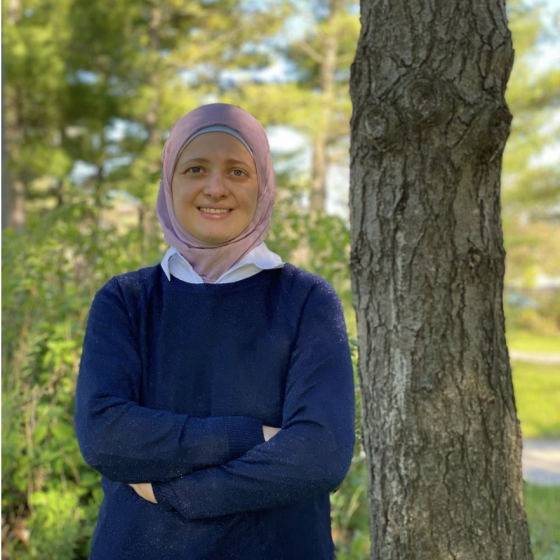 A person in a blue shirt and head scarf standing next to a tree