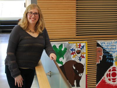 Brock student Lianna Manes standing beside banners painted in a class
