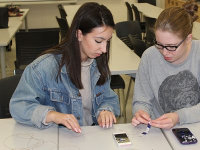 Two Brock students work on beading sections of a Two Row Wampum Belt