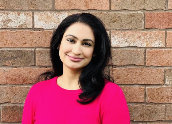 A woman stands in front of a brick wall smiling.