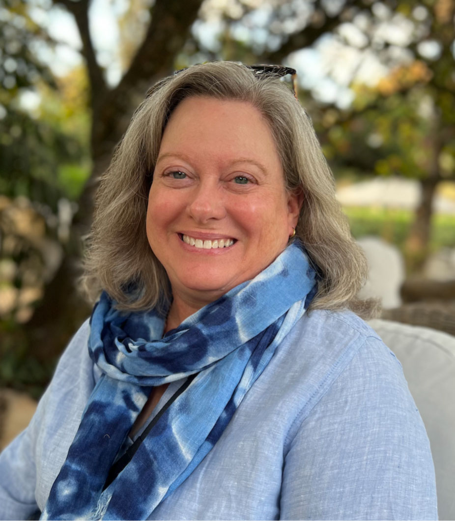 A woman smiles at the camera while sitting outside.
