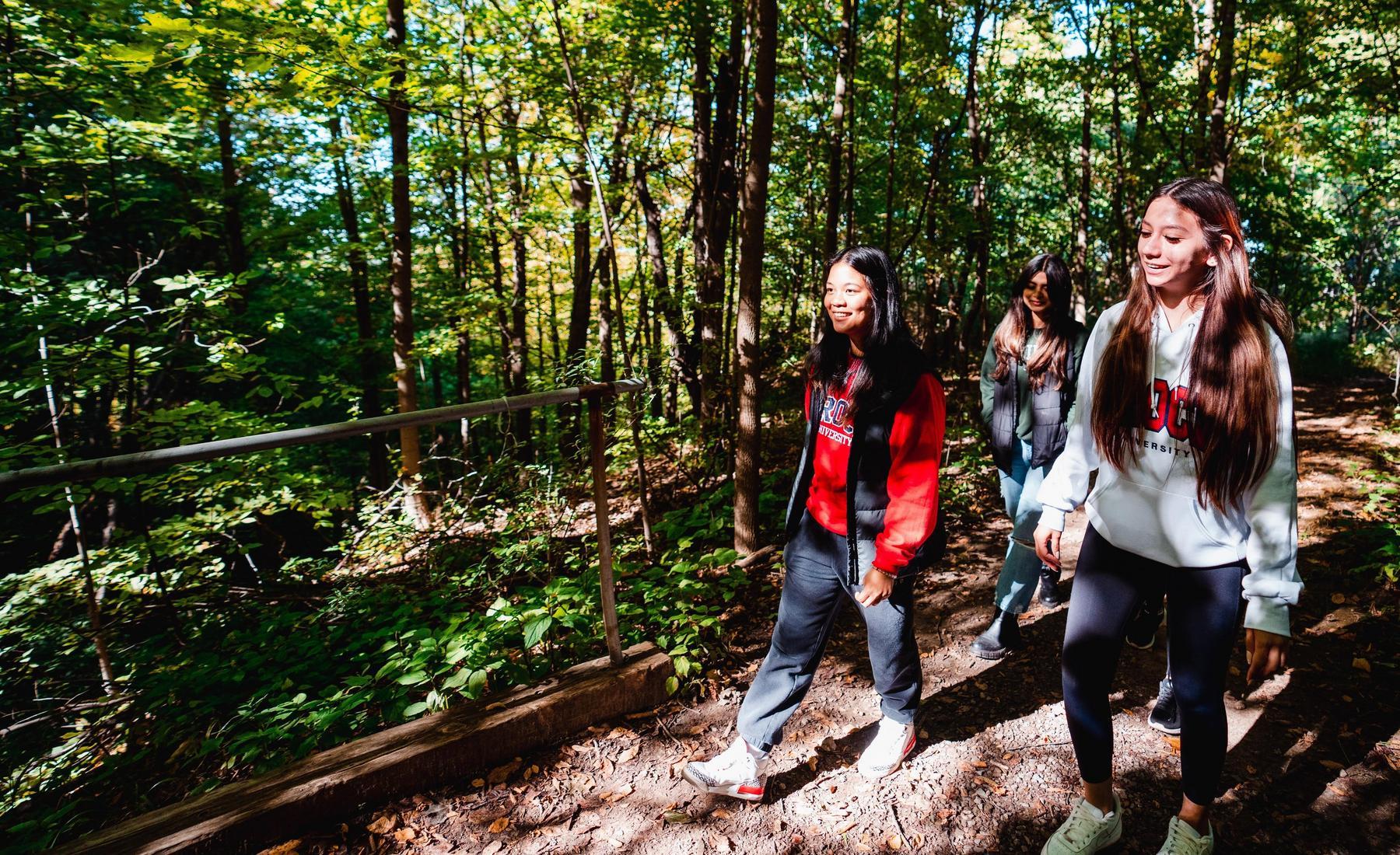 Three students in Brock University sweaters walking on a trail in the woods. 