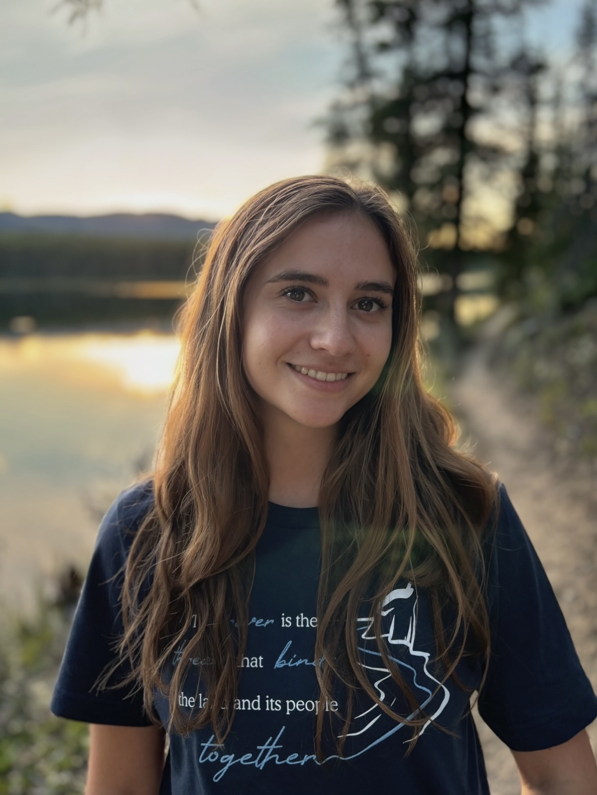 Kaila's Headshot Photo Kaila Belovich standing in front of a sunlit lake.