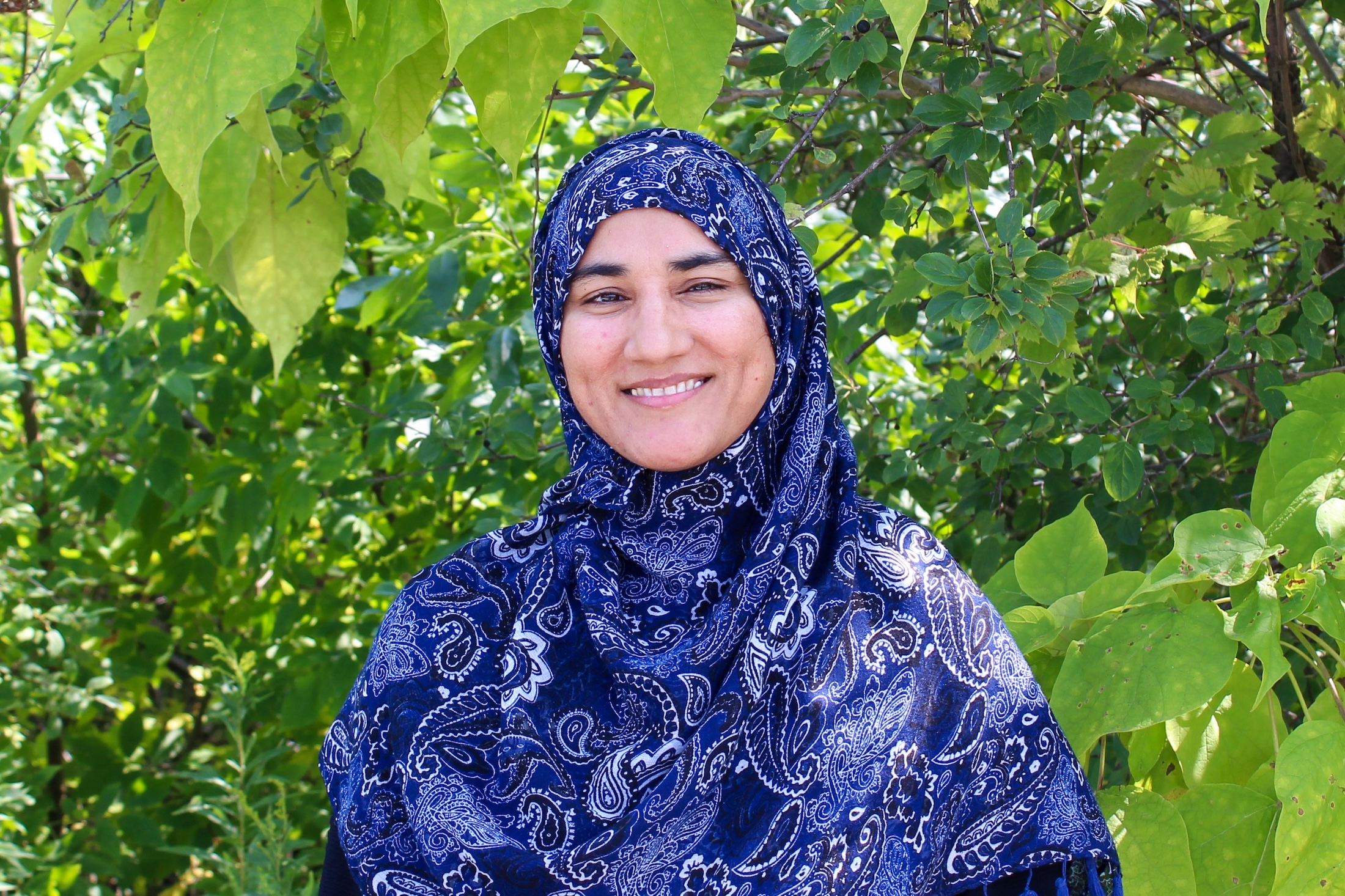 Uzma Final Uzma Bibi standing in front of trees.