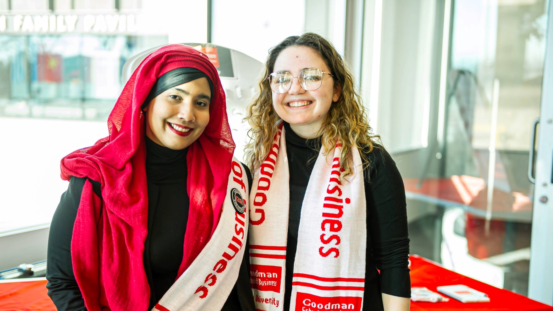 Two business students smile wearing Goodman School of Business scarves. 