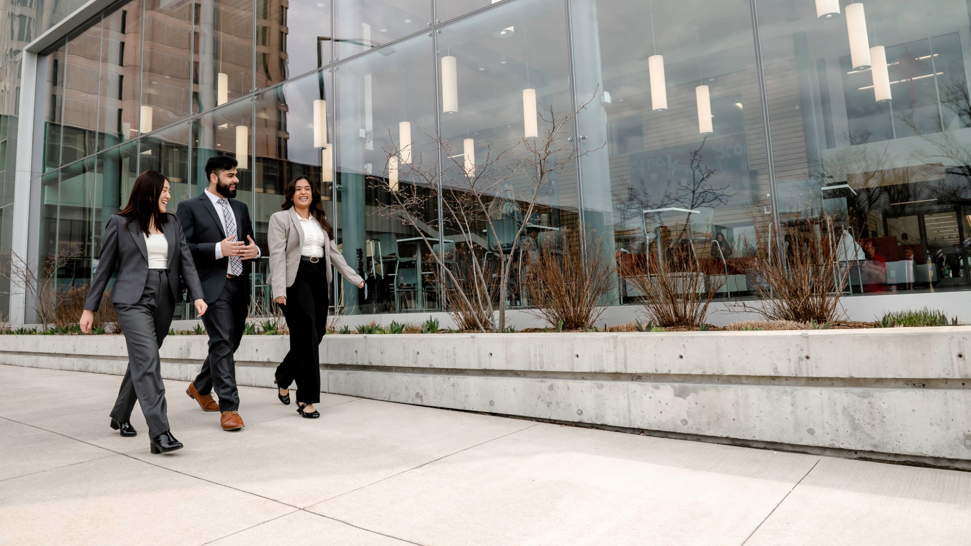 Three business students walk in front of the Goodman School of Business building. 