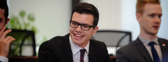 Goodman undergraduate student in professional business attire sitting next to two students at a table.