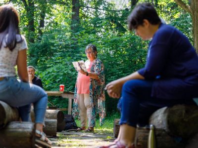 A gathering of people around a fire listen to an author read her book.