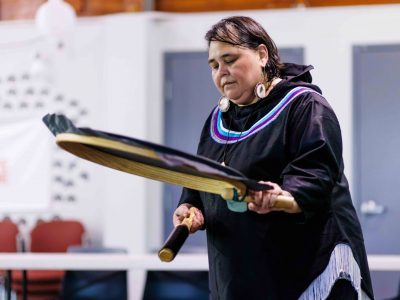 Inuk women in traditional regalia plays hand drum.