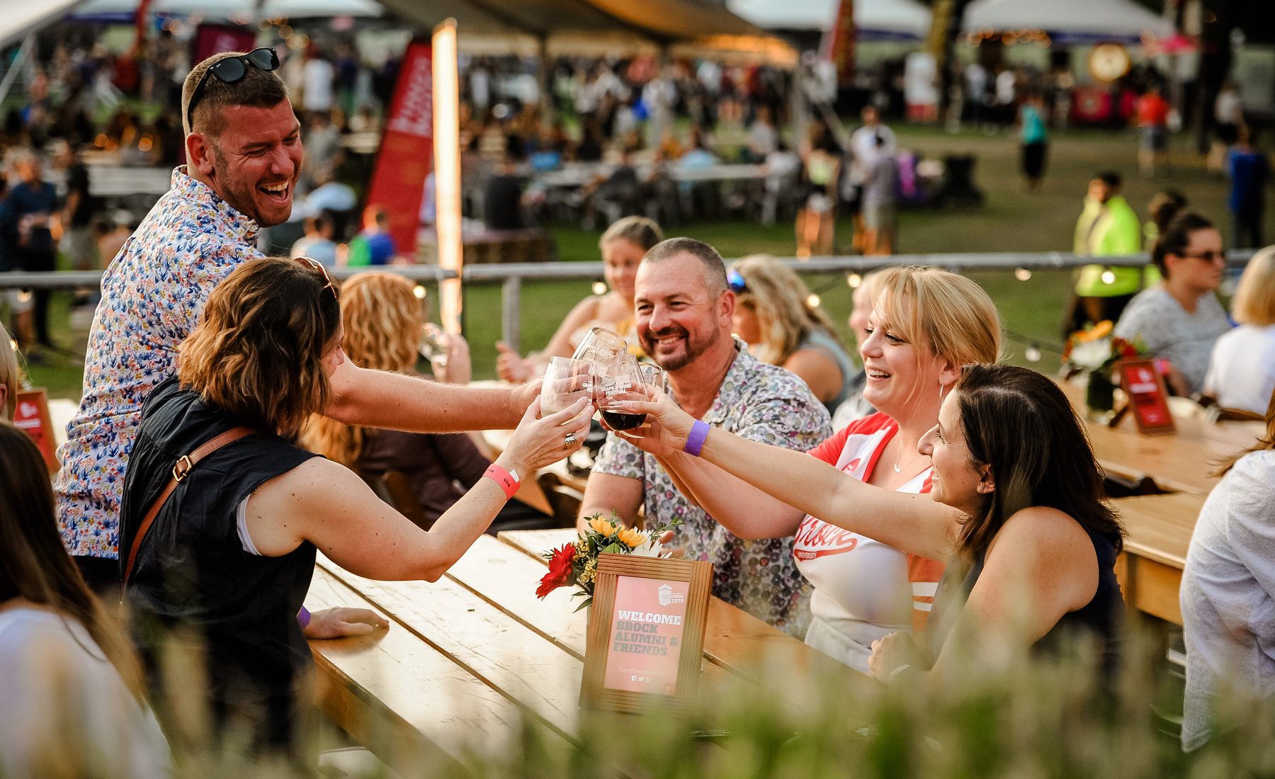 Group of adults laughing and clinking glasses at outdoor festival 