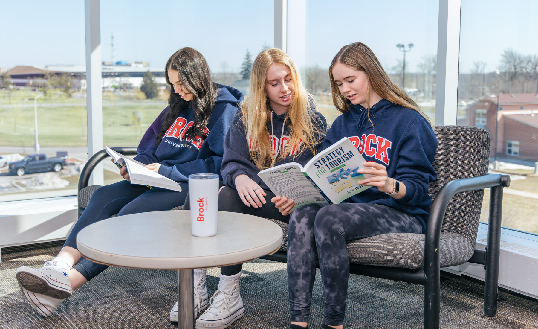 Three students sitting looking at and discussing a textbook