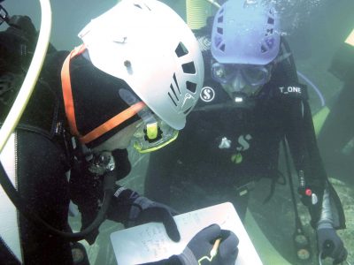 2 scuba divers writing on tablet underwater