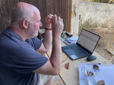 professor at wooden desk with laptop cataloging artifacts