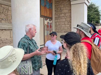 6 students look at professor at a column and building in Gournia