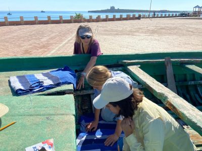 3 archeologist students in an ancient wooden boat