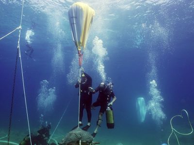 2 scuba divers lifting an artifact underwater balloons