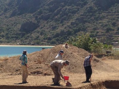 5 archeology students in hats sifting through sand