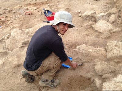 archeology student in hat sifting through sand
