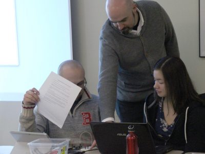 professor pointing to laptop screen of 2 students