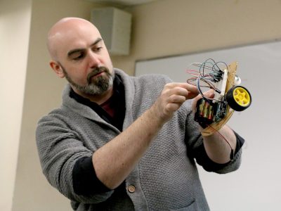 professor holding a robot with wheels