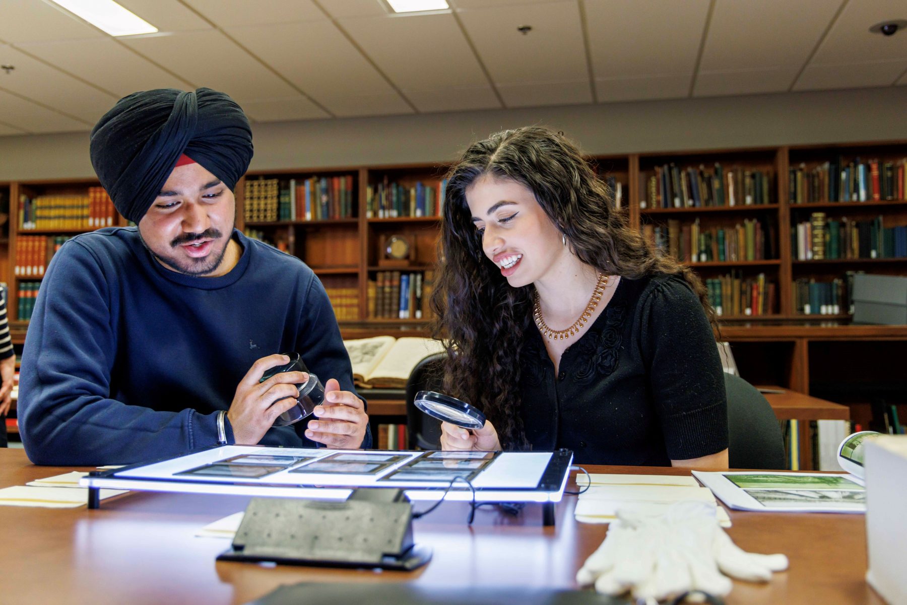 Male student wearing turban and female student with long hair examine photos on a light table