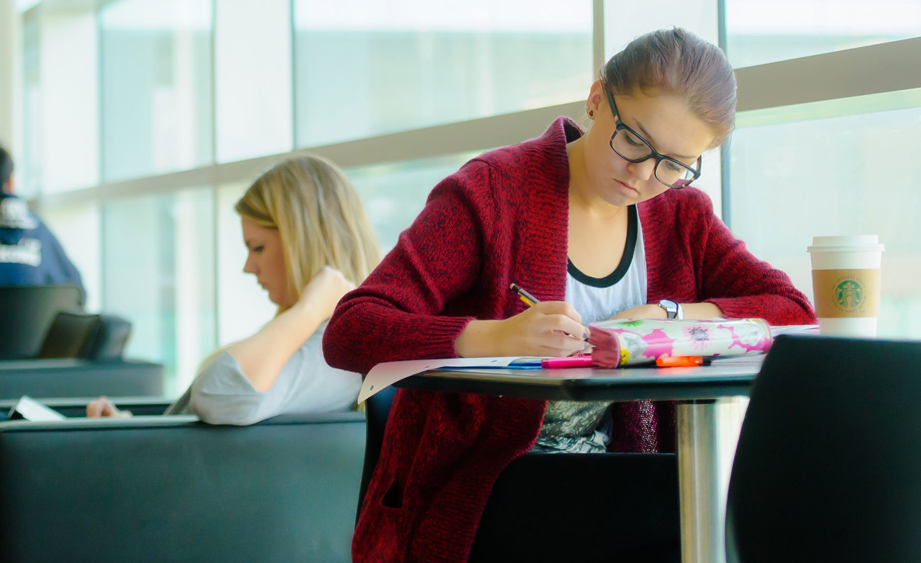 student in red sweater and glasses writing at table