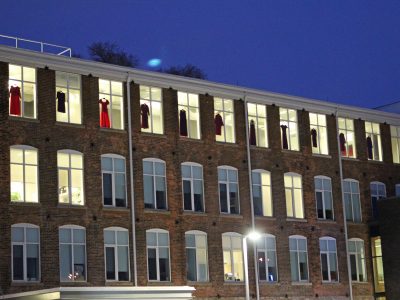 a view from outside of MIWSFPA building red dresses hanging from windows inside hallway by windows