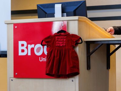 A infant sized red dress hangs on a podium.