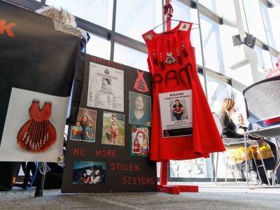 An exhibit for missing Indigenous women and girls. A red dress hangs in the center next to a poster board, with the text 