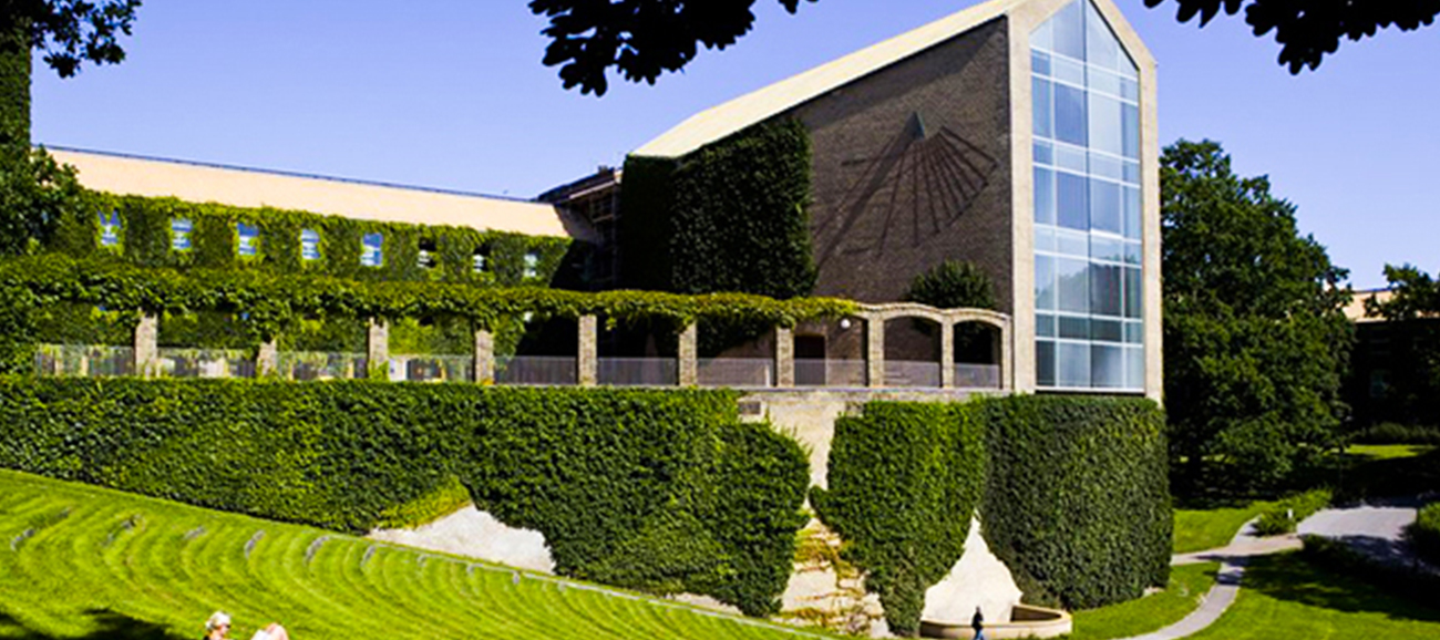 An ivy-covered building in a lush green courtyard on a sunny day at Aarhus University in Denmark.