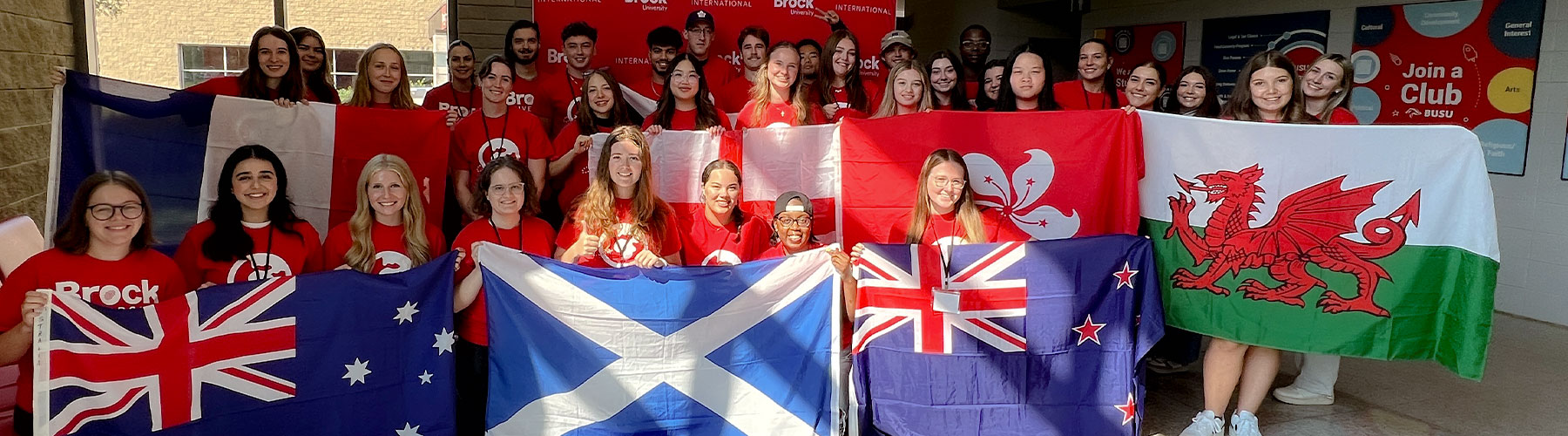A group of university students pose for a group photo holding flags from countries around the world.