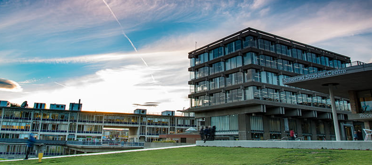 A modern glass building set against a pink and blue clouded sky.