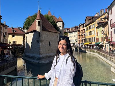 A woman smiles at the camera on a bridge in front of a canal.